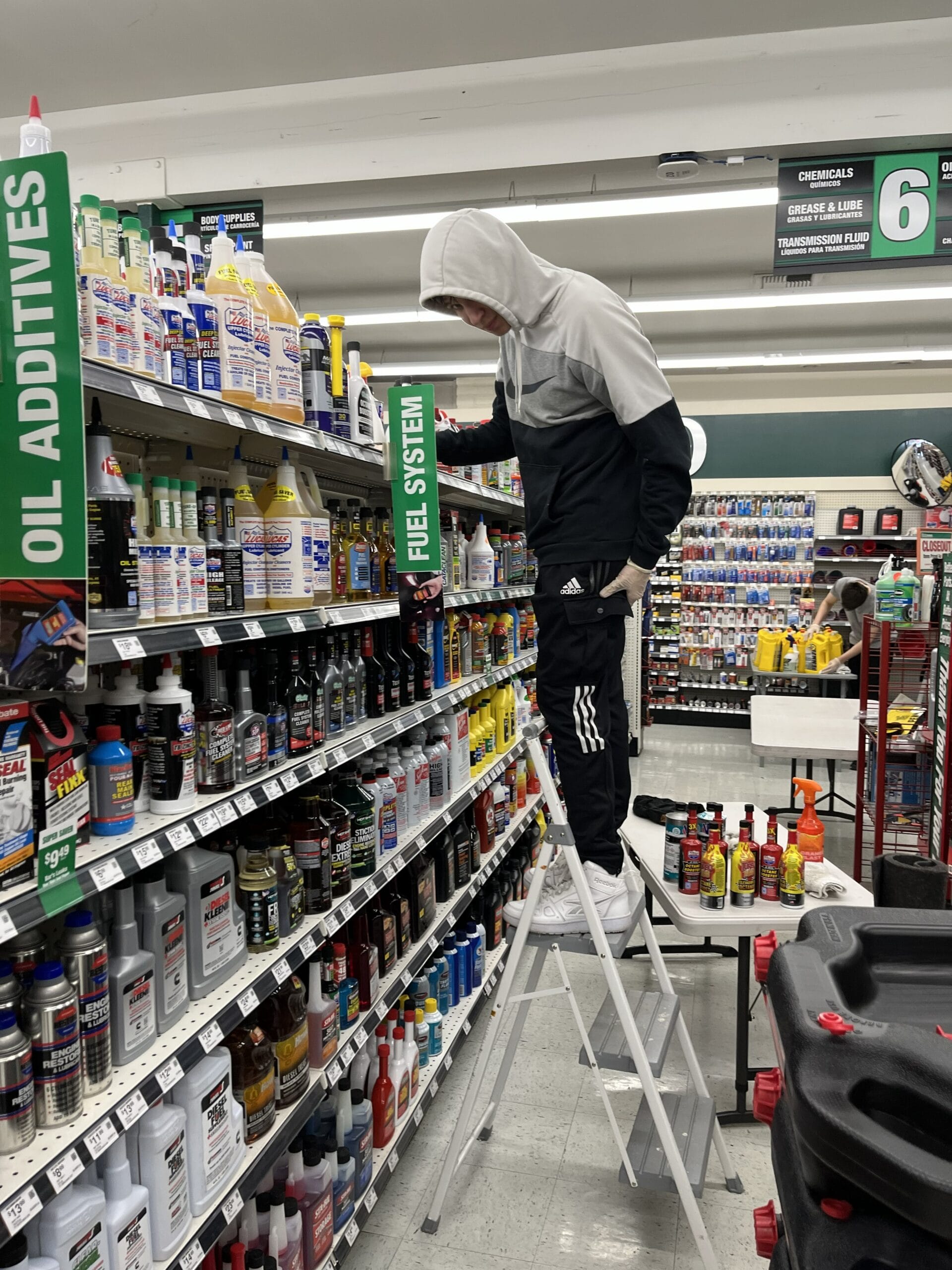 Commercial cleaner using a step ladder to clean upper retail shelves